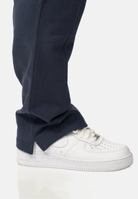 Navyblaue Jogginghosen mit lockerem Schnitt, kombiniert mit weißen Ledersneakern, die über perforierte Details und eine strukturierte Sohle verfügen.