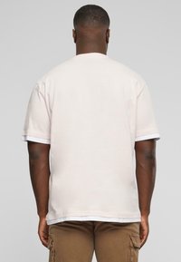 Lys pink t-shirt med en afslappet pasform, korte ærmer og ribbet halsudskæring. Stoffet ser blødt ud, med en ensartet tekstur og ingen synlige mønstre.