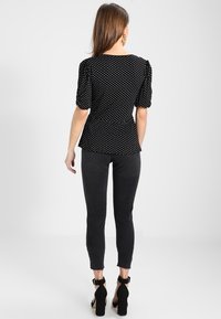 Svart blus med polka prickar och puffärmar, peplum midja, tillverkad av lättviktsmaterial. Sammanfogas med svarta smala jeans och klackskor med ankelsnodd.