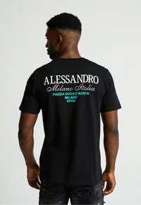 Camiseta de algodón negra con texto blanco y turquesa en la parte posterior. El texto incluye "ALESSANDRO," "Milano Italia," y detalles de ubicación.