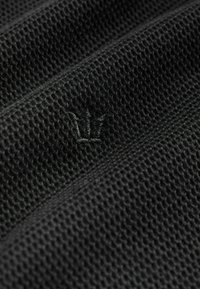 Schwarzer Mesh-Stoff mit einer strukturierten Oberfläche und einem dezenten gestickten Kronenlogo. Das Material ist leicht und atmungsaktiv.