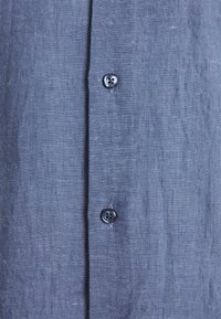 Camicia in lino blu navy con chiusura a bottoni, dotata di due bottoni in plastica nera e una superficie di tessuto stratificato.