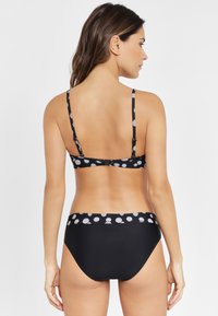 Bikini negro con tirantes finos y un patrón de lunares en la parte posterior. La parte inferior tiene un diseño negro sólido con una cinturilla estampada.