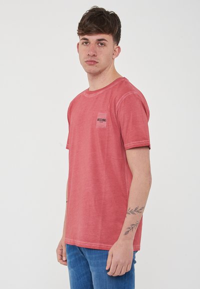 T-shirt in cotone lavato rosso con collo tondo e maniche corte. Presenta un piccolo patch di marca sul lato sinistro del petto e una vestibilità rilassata.