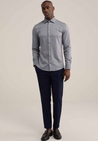 Camisa de botón gris de manga larga con cuello puntiagudo, combinada con pantalones marinos y mocasines negros. Textura suave, diseño ajustado.
