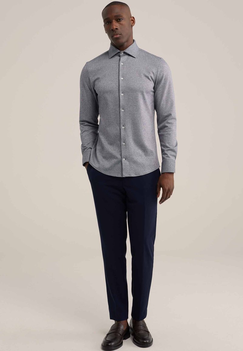 Camisa de botón gris de manga larga con cuello puntiagudo, combinada con pantalones marinos y mocasines negros. Textura suave, diseño ajustado.