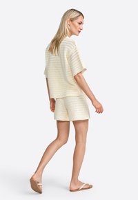Cream-colored crochet knit set featuring a loose-fit top with short sleeves and matching shorts, paired with flat sandals.