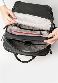 Zwarte rugzak met een gestructureerde buitenkant, dubbele ritssluiting en een grijs geruit interieur met meerdere organisatievakken.