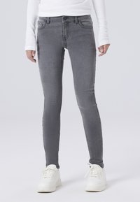 Šedé skinny džíny z elastického materiálu, s poutky na pásek, předními kapsami a zapínáním na knoflík. Stylizované s bílými teniskami.