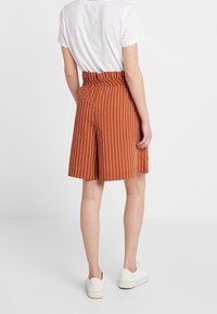 Pantalones cortos a rayas marrones con un diseño de cintura alta, pliegues a medida y una textura suave, combinados con zapatillas blancas.