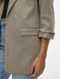Lys grå blazer med teksturert stoff, enkelt frontlomme og oppbrettede ermer, kombinert med falmede blå jeans.