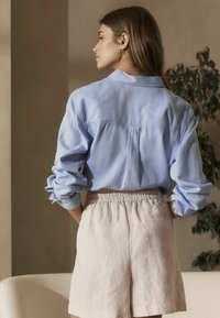 Helles blaues Hemd mit aufgerollten Ärmeln, Rückenpasse und lässigem Schnitt. Kombiniert mit weichen, rosa Leinen-Shorts mit elastischem Bund.
