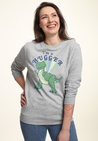 Grå sweatshirt med en grön dinosaurie-grafik och texten "Jag är en kramare." Ribbad mudd och nederkant, mjukt tyg, avslappnad passform.