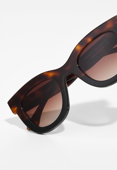 Lunettes de soleil en écaille avec un design chunky et surdimensionné. Verres dégradés marron, texture lisse et logo subtile sur le bras intérieur.
