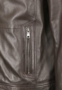 Bruine leren jas met een ritszak aan de zijkant, een gladde textuur en nette stiksels langs de naden.