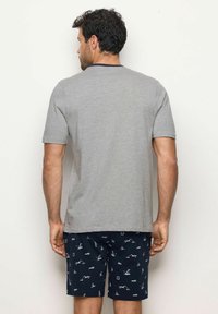 Camicia grigia a maniche corte con scollo rotondo, abbinata a pantaloni corti blu navy con un motivo nautico di barche e ancore.