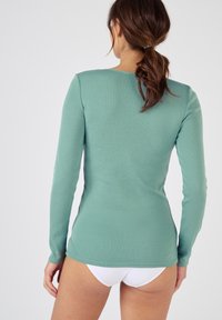 Langsleeve, getailleerd shirt van zacht, gestructureerd mintgroen stof, met een ronde halslijn en een langere achterzoom. Gepaard met een witte onderkant.