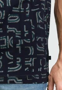 Navy T-shirt featuring a geometric pattern in white and teal, with distinct curved and straight lines. Cotton fabric, tag visible at the side.