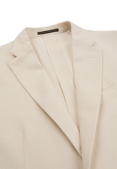 Roomkleurig gestructureerd colbert met ingesneden revers en een borstzak, plat gelegd op een witte achtergrond.