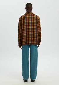 Geruit flanellen overhemd in oranje en bruine tinten, met blauwe accenten. Gecombineerd met loszittende blauwe spijkerbroek. Zichtbare achterzijde ontwerpdetails.