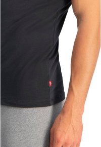 Tricou negru cu mânecă scurtă, din bumbac, cu decolteu rotund. Prezintă un mic etichetă roșie cu logo-ul Levi's pe cusătura laterală.