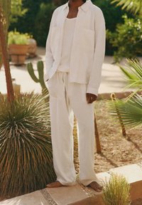 Hvid hørskjorte med to forlommer og matchende bukser med bindebånd. Blød tekstur, afslappet pasform og minimalistisk design.