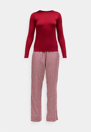 Maglietta rossa a maniche lunghe abbinata a pantaloni da pigiama a scacchi rossi e bianchi. La maglietta è aderente; i pantaloni sono larghi con una cintura elastica.