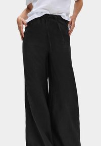 Czarne spodnie szerokie wykonane z lekkiego materiału z elastycznym paskiem ściągającym w talii i gładką teksturą. Odpowiednie na codzienne wyjścia.
