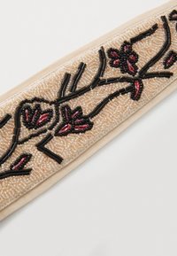 Bandă de cap din țesătură cu mărgele, cu un fundal crem și modele florale complexe în nuanțe de negru și burgund. Textură netedă, cu o bandă flexibilă.