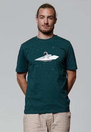 Donkergroene katoenen T-shirt met een witte afbeelding van een astronaut op een papieren vliegtuigje tegen een stervende achtergrond. Korte mouwen, ronde halslijn.