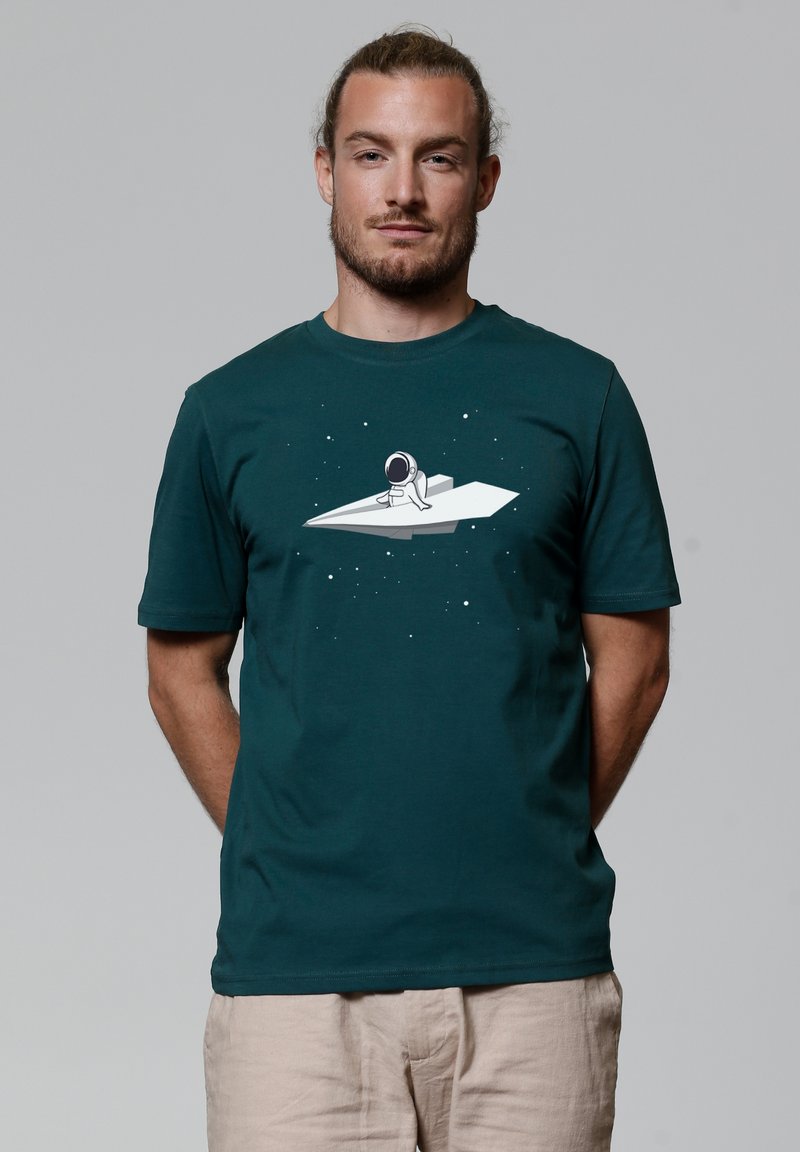 Dunkelgrünes Baumwoll-T-Shirt mit einem weißen Motiv eines Astronauten auf einem Papierflieger vor einem sternenübersäten Hintergrund. Kurze Ärmel, runder Halsausschnitt.