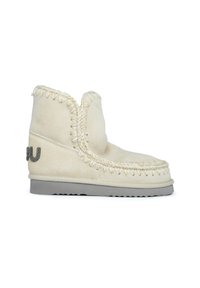 Botas de ante crema con costuras decorativas, parte superior redondeada y suela texturada en gris. Presenta un detalle de logo en gris metálico en un lado.