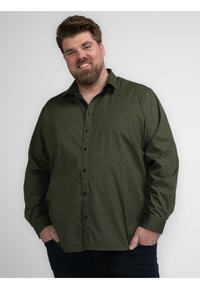 Camisa abotonada de patrón verde con mangas largas, botones negros y una textura suave. Presenta un diseño geométrico en toda la tela.