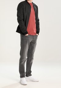 Giacca bomber nera, t-shirt rossa, jeans grigi e sneakers bianche, con giacca texturizzata, pantaloni a gamba dritta e calzature casual.