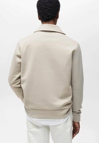 Felpa beige con un ampio colletto, polsini e orlo a coste. Realizzata in materiale morbido, presenta un design pulito e dettagli di cucitura sobria.