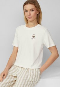 Witte katoenen t-shirt met korte mouwen, met een cupcake en "SWEET LIKE A CUPCAKE" geborduurd in het zwart. Gecombineerd met gestreepte beige broek.
