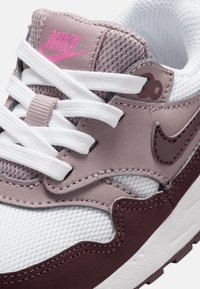 Teniska Nike s šedým a bílým síťovinovým svrškem, levandulovými semišovými akcenty, růžovým logem, bílými tkaničkami a texturovanou gumovou podešví.