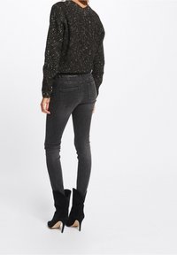 Black, textured sweater with metallic specks, paired with dark grey skinny jeans and black high-heeled ankle boots. View from the back.