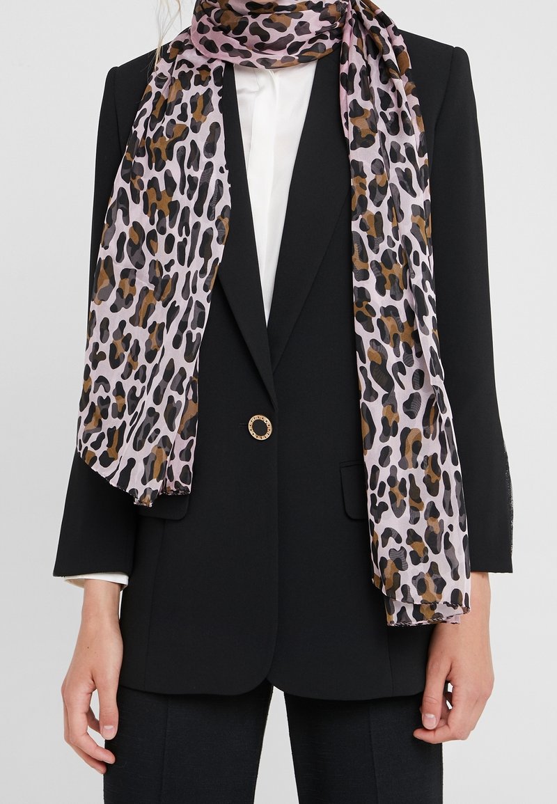 Écharpe à imprimé léopard en violet clair, marron et noir, drapée sur une chemise blanche et un blazer noir avec un seul bouton doré.