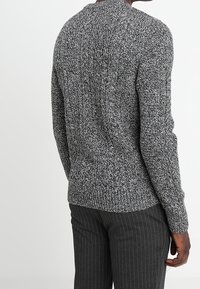 Grå stickad tröja med ett strukturerat mönster, med rund halsringning och figursydd form. Kombinerad med mörka byxor med kritstrecksrand.