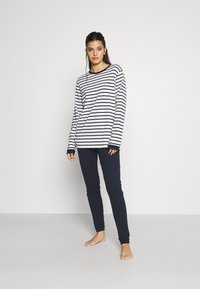 Fosă lungă cu dungi în alb și bleumarin, cu un mic logo roșu, asortată cu pantaloni bleumarin slim-fit, dintr-un material moale.