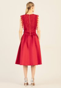 Rotes Kleid mit einem Spitzenoberteil mit gewelltem Saum, einer taillierten Taille und einem satinierten Rock. Enthält einen Reißverschluss auf der Rückseite und silberne Absätze.