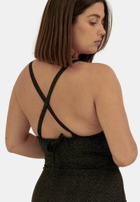 Jumpsuit noir scintillant avec des bretelles croisées, présentant un dos nu et un tissu texturé. Détail de lien adjustable à la taille.