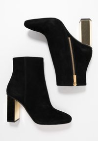 Botines negros de ante hasta el tobillo con punta afilada, cierre dorado con cremallera y un tacón robusto acentuado en dorado, con una textura suave.