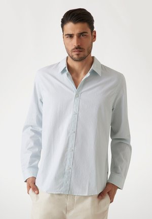 Chemise à rayures bleues claires et blanches à manches longues avec un devant à boutons, un col et une texture douce, stylisée avec une coupe décontractée.