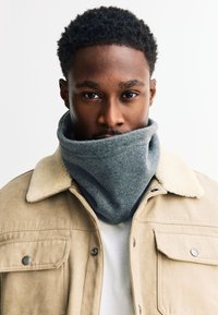 Szürke polár nyakmelegítő, bézs színű ingdzseki fölött, melynek műszőrmés gallérja van. Simaság jellemzi, kerekded formájú, nyak körül szorosan illeszkedik.