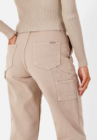 Beige cargobroek met meerdere zakken, een ontspannen pasvorm en een gestructureerde stof, gecombineerd met een geribbelde, lichtgekleurde lange mouwtop.