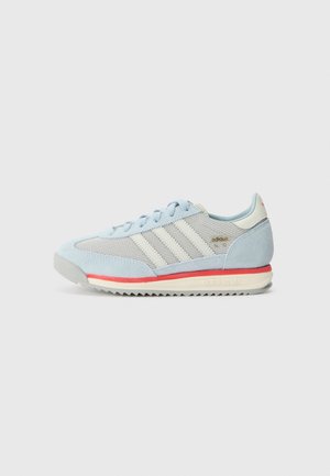 Jasnoniebieski sneaker Adidas z białymi paskami, cholewką z siatki i zamszu, czerwonym akcentem na podeszwie oraz szarą podeszwą zewnętrzną w zygzak, widok z boku.