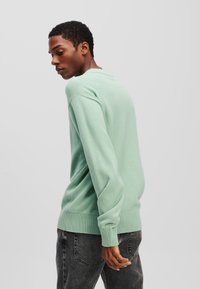 Mintgrøn strikket sweater med lange ærmer, rund halsudskæring og ribkantede manchetter og kant; parret med mørkegrå jeans.