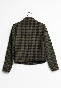 Villa takki, jossa on tummanvihreä ja musta houndstooth-kuvio, kaulus, pitkät hihat ja lyhennetty takasauma. Ripustettu koukkuun.